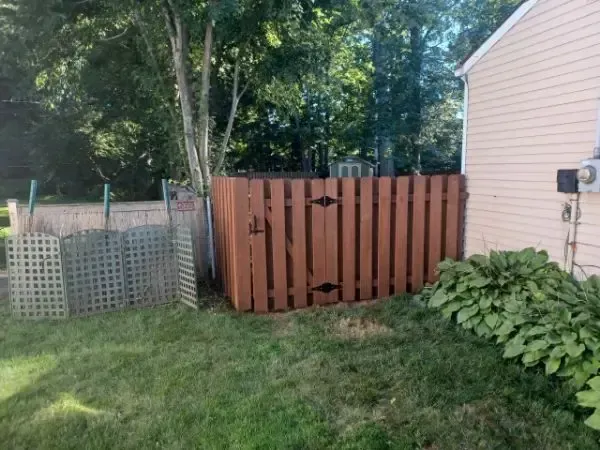 Backyard with a broken wooden fence section beside a house, trees, and lawn grass.