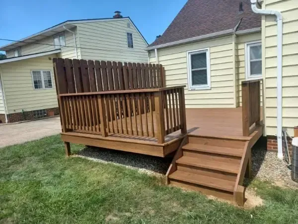 Small wooden backyard deck with stairs and railing beside a beige house