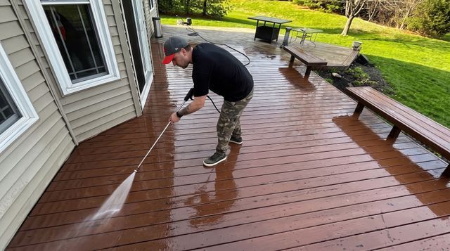 Person pressure washing a driveway beside trimmed bushes and a house