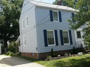 White two-story house with blue shutters and siding, viewed from the street on a sunny day