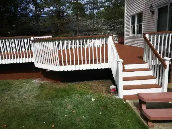 Wooden deck with white railings and stairs beside a house, overlooking a grassy yard.