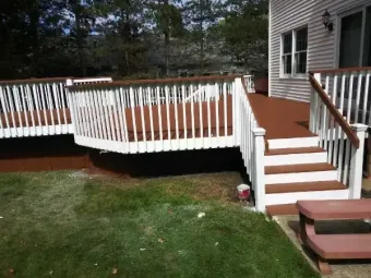 Wooden deck with white railings and stairs beside a house, overlooking a grassy yard.
