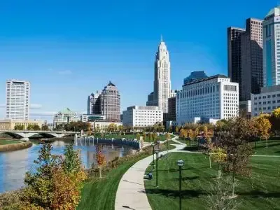 City skyline beside a river and green park under a clear blue sky