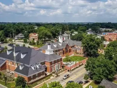 Aerial view of a red-brick campus building with gray roofs, trees, and a road beside it