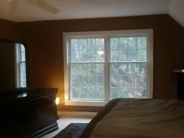 Bedroom with window and dresser, softly lit by warm light, bed in foreground
