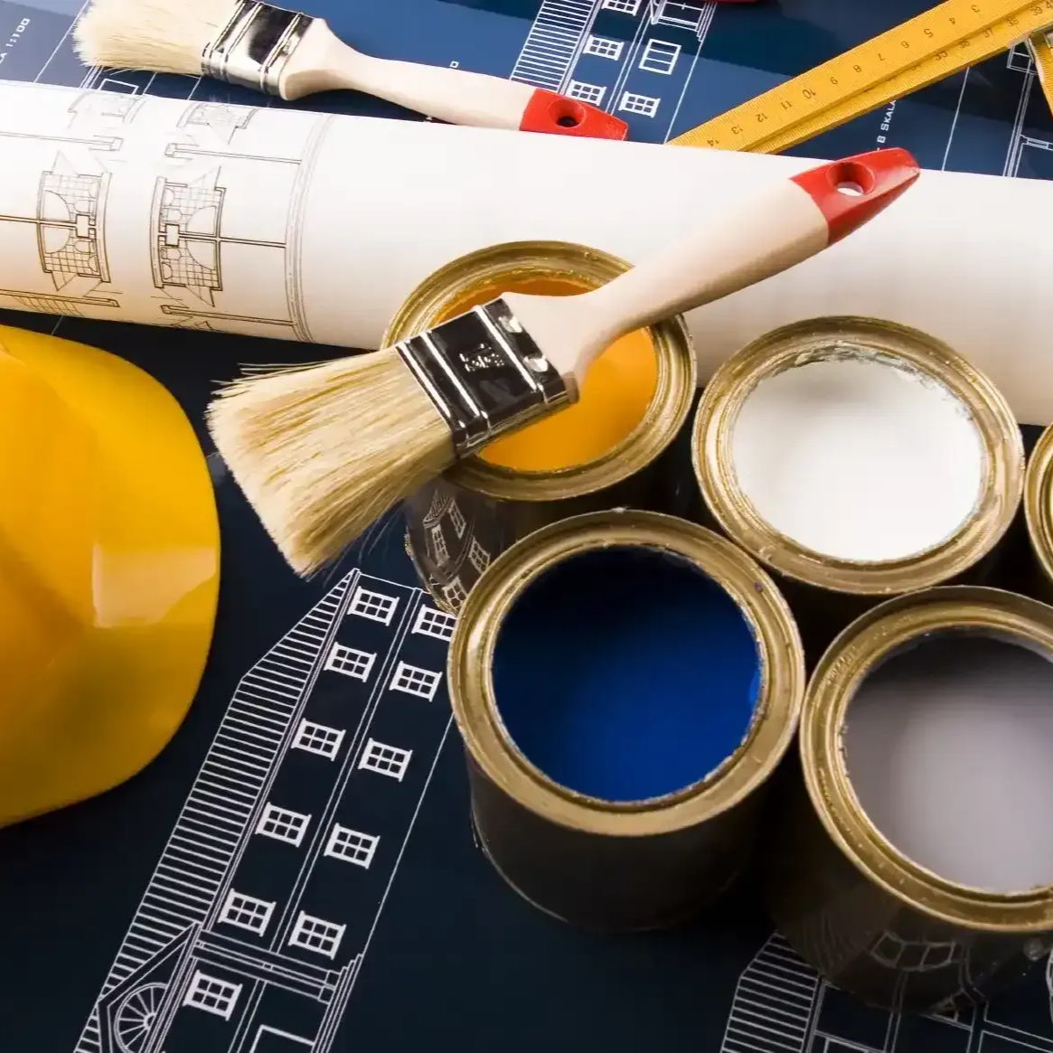 Paintbrushes, rolled blueprints, and open paint cans on a worktable with a measuring tape