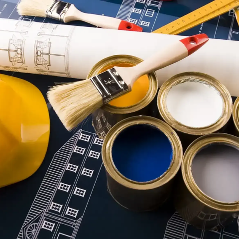 Paintbrushes, rolled blueprints, and open paint cans on a worktable with a measuring tape