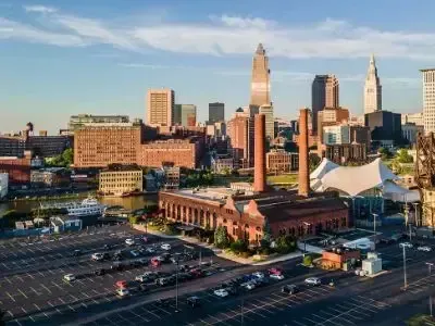 City skyline at sunset with downtown buildings, parking lot, and a white tent near the waterfront.