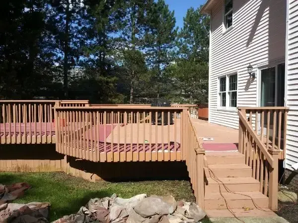 Wooden deck with steps beside a house, overlooking a grassy yard and trees.