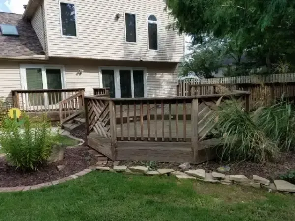 Backyard with a wooden deck, stone border, lawn, and a house exterior in the background