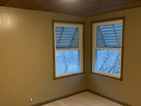 Empty beige room with two corner windows and blue shutters.