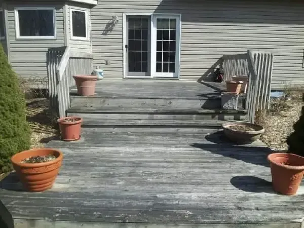 Weathered wooden deck with potted plants, steps, and sliding glass doors on a house patio