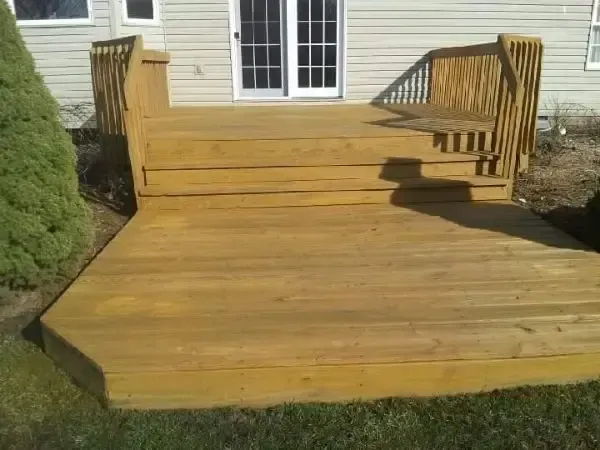 Wooden front porch deck with steps and railings, leading to sliding glass doors on a house