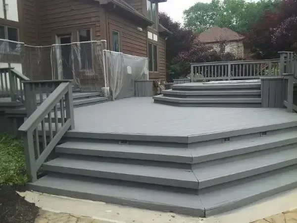Gray multi-level wooden deck with railings beside a house and laundry line in a backyard