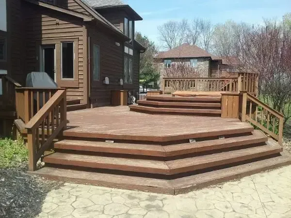 Wooden deck with wide steps and railings beside a house, overlooking a backyard.
