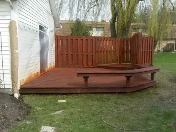 Backyard wooden deck with built-in bench and fence beside a white house