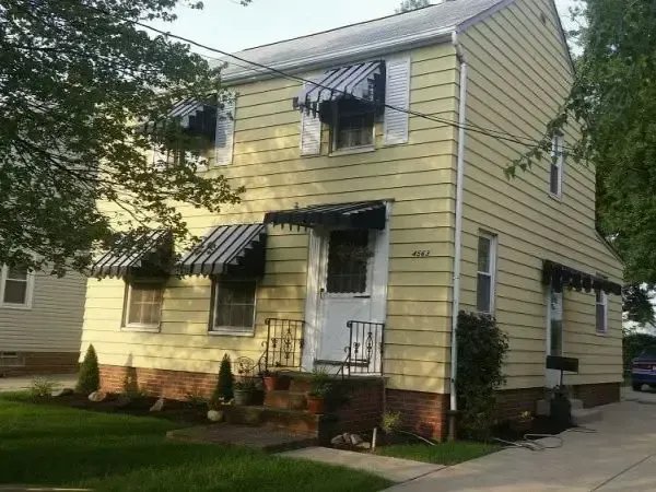Yellow two-story house with black awnings and white porch, viewed from the front