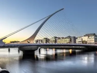 Modern cable-stayed bridge at sunset over calm water with city buildings in the background