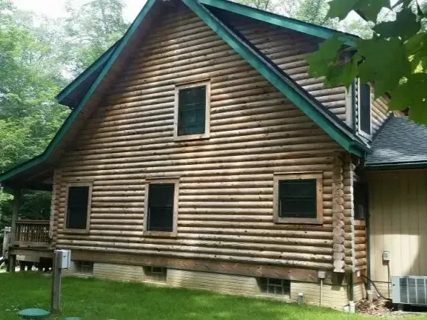 Log cabin-style house with log siding, green trim, and multiple windows in a wooded area