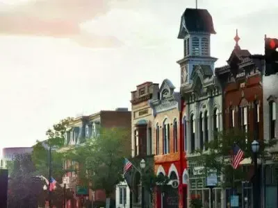 Historic storefronts on a colorful main street with American flags and a tower at dusk