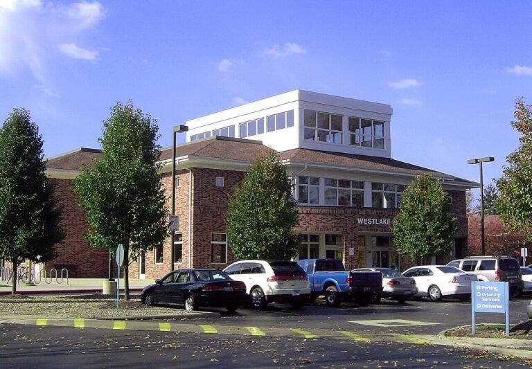 Brick public building with parking lot, several cars, and a blue sky
