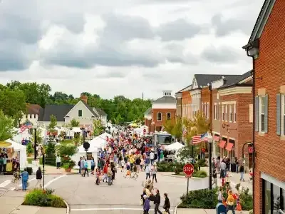 Crowded street fair in a small downtown with tents, brick buildings, and cloudy skies