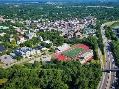 Aerial view of a suburban neighborhood with a sports field, trees, and a highway on the right