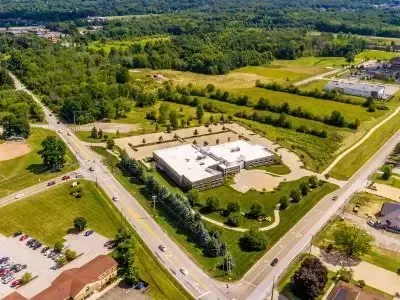 Aerial view of a white office building with parking lots, roads, and green trees in a suburban area