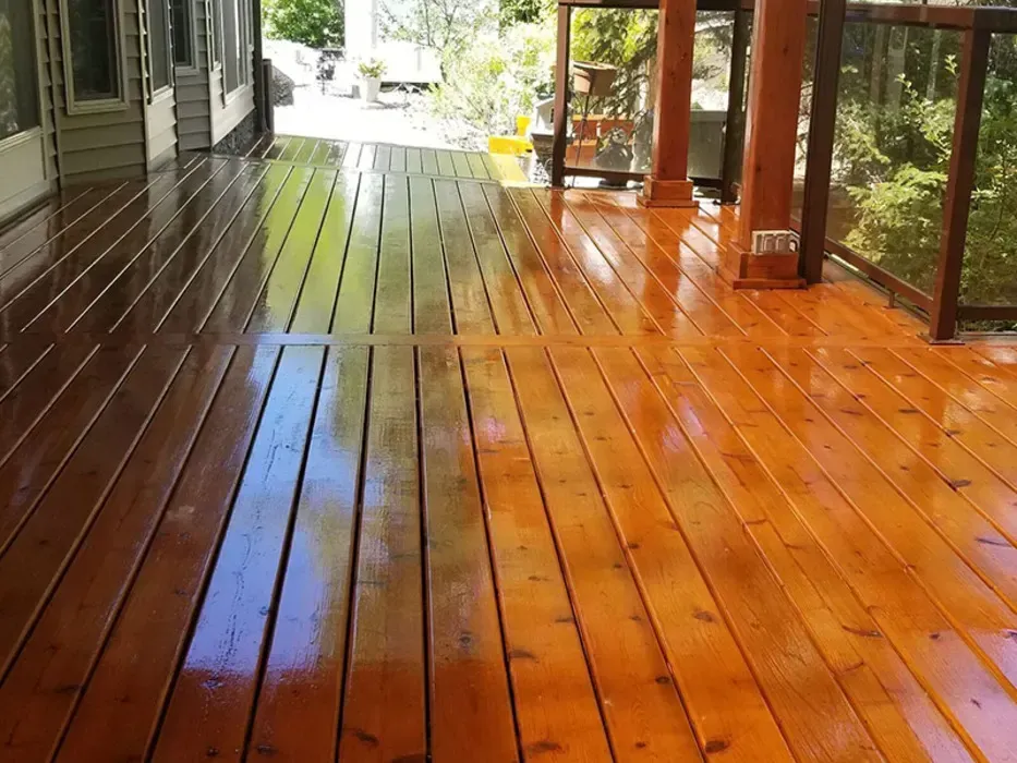 Wooden porch deck with wet, glossy boards and a screened seating area overlooking greenery