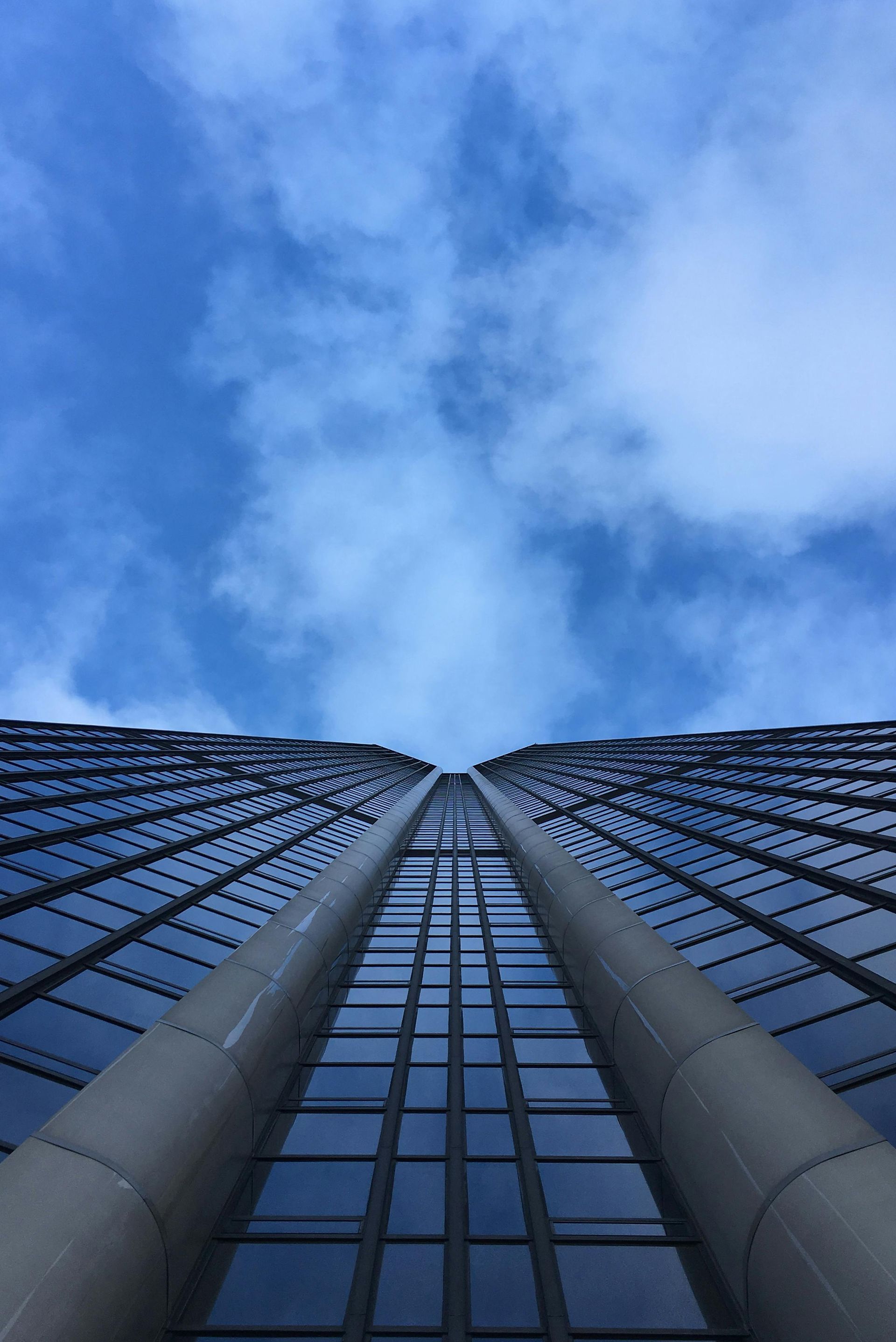 Gratte-ciel imposant, ciel bleu au-dessus, vu du sol. Vitrages, colonnes de soutien grises.