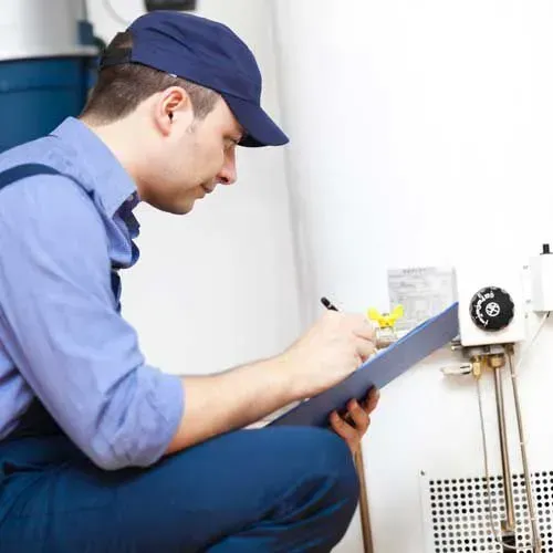 A man is kneeling down in front of a water heater.