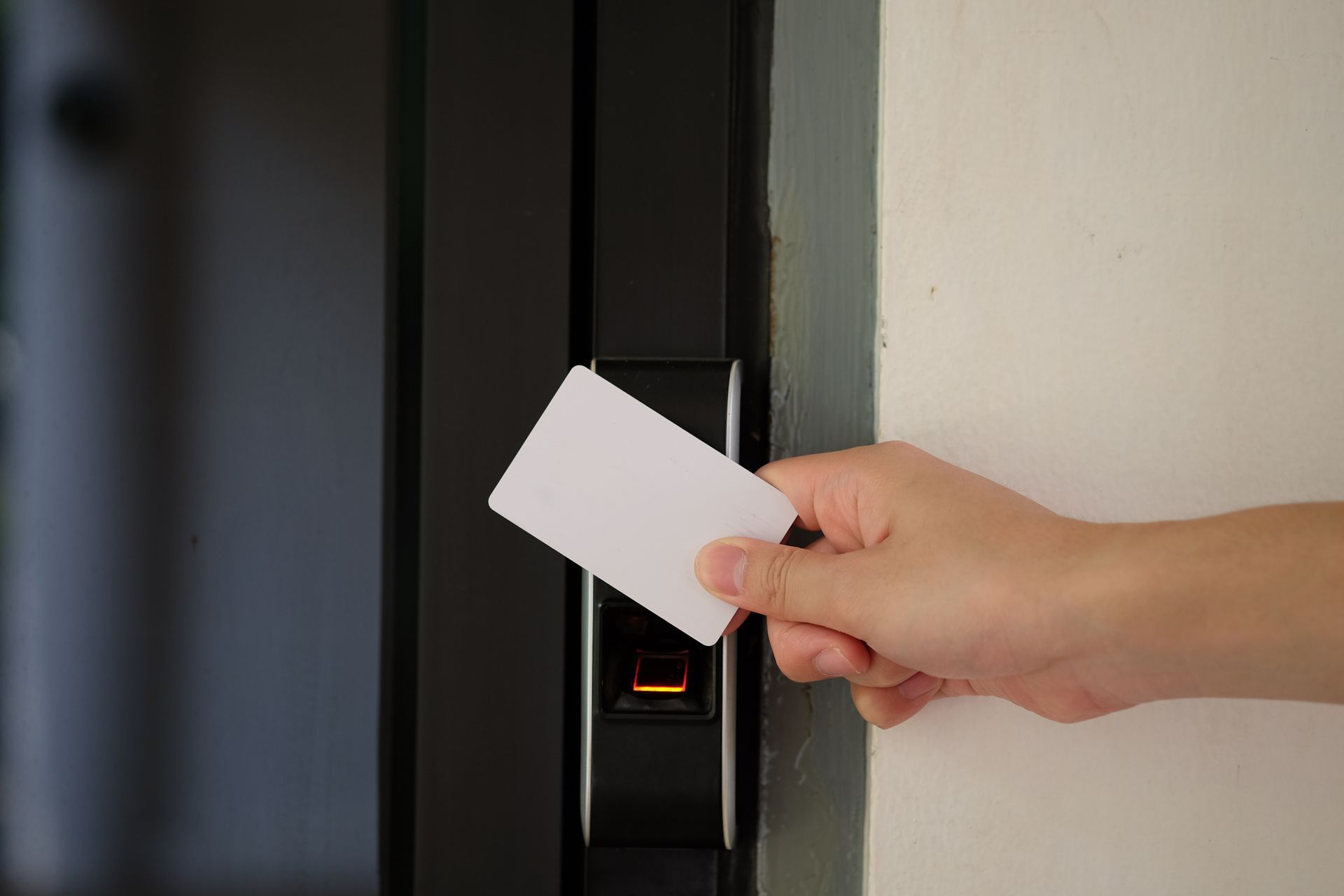 A person is holding a white key card to unlock an electronic access control door.