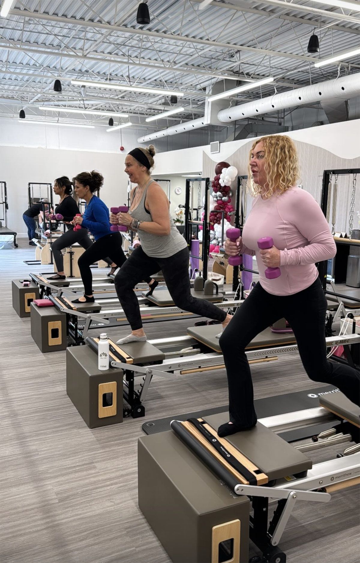 People doing lunges with weights on pilates machines in a gym.