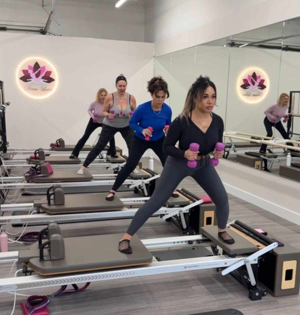 Pilates class: women exercising with weights on reformer machines in a studio.