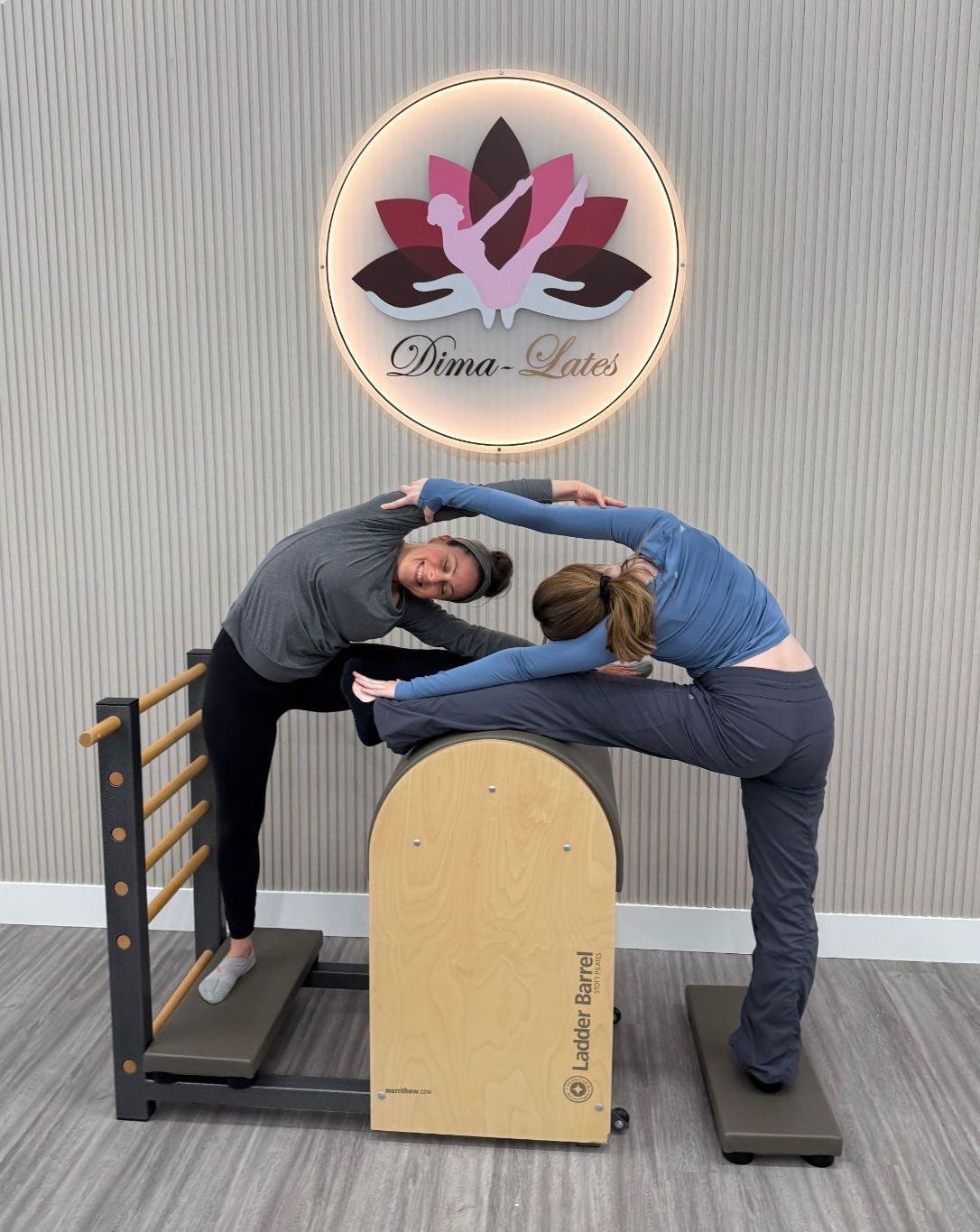 Two people stretching on Pilates equipment beneath a studio logo.
