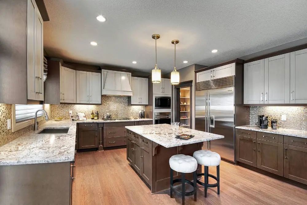 Kitchen with light-colored cabinets, brown island, and granite countertops. Two pendant lights hang above the island.