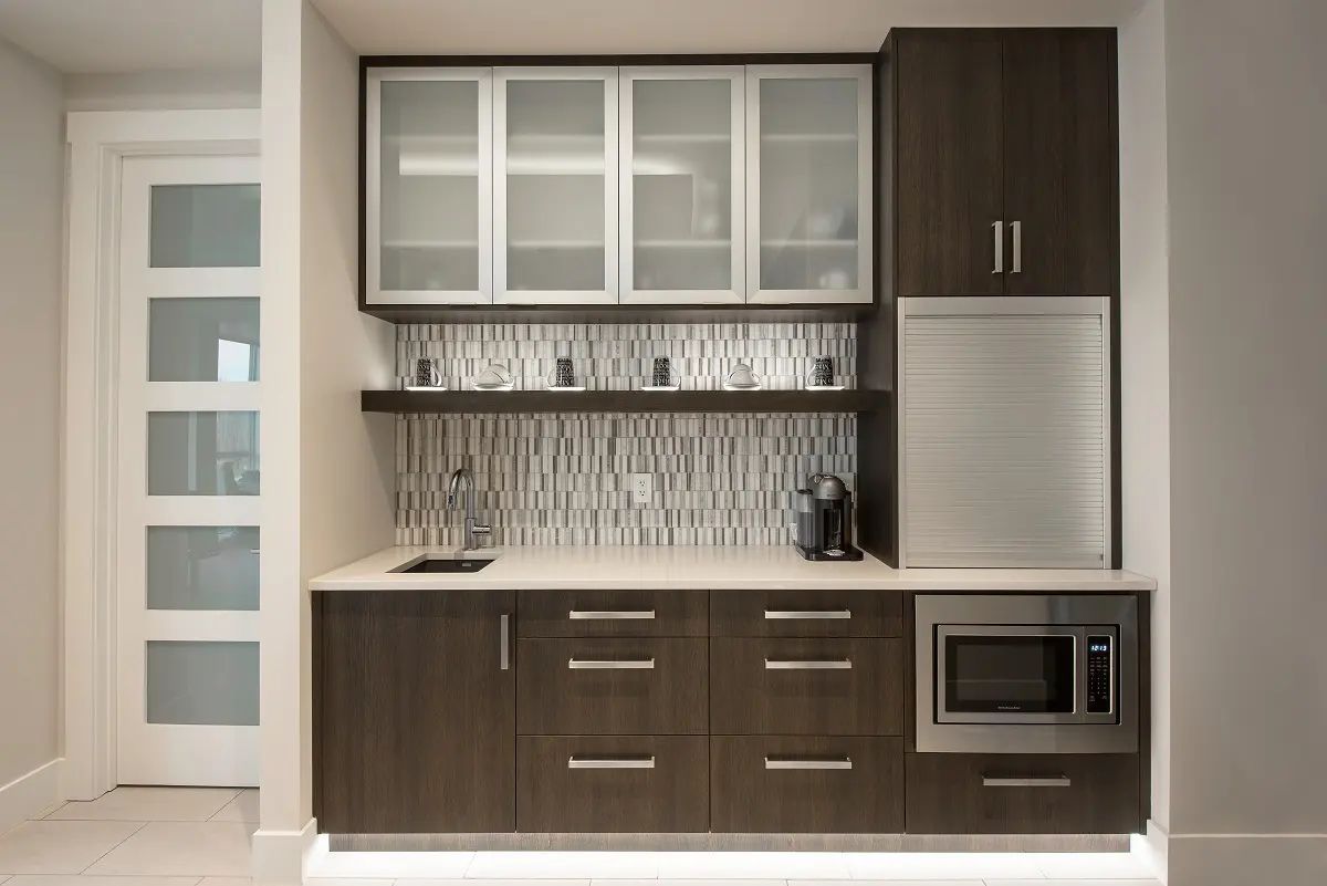 Modern built-in bar with dark wood cabinets, frosted glass uppers, stainless steel appliances, and a mosaic backsplash.