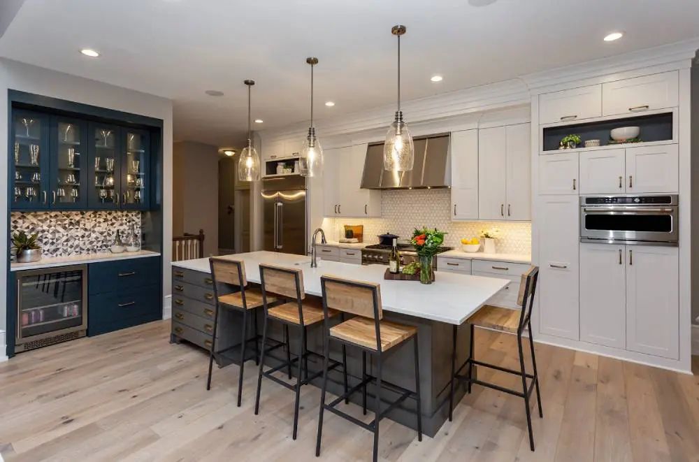 Modern kitchen with island, cabinets, and appliances. Blue and white color scheme, light wood floors, pendant lights.
