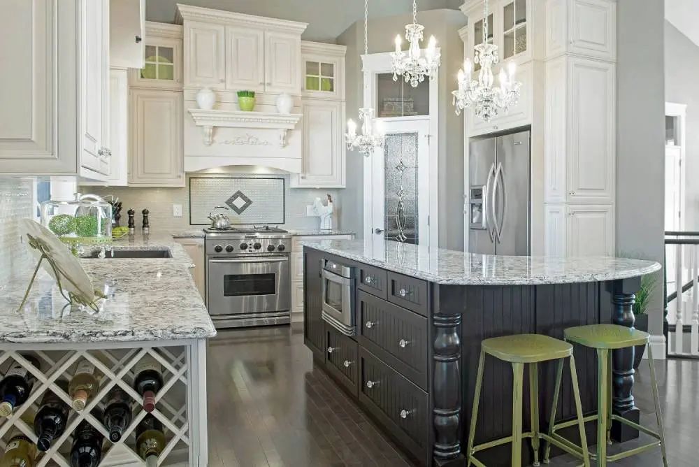 Elegant white and dark wood kitchen with granite countertops, stainless steel appliances, and two chandeliers.