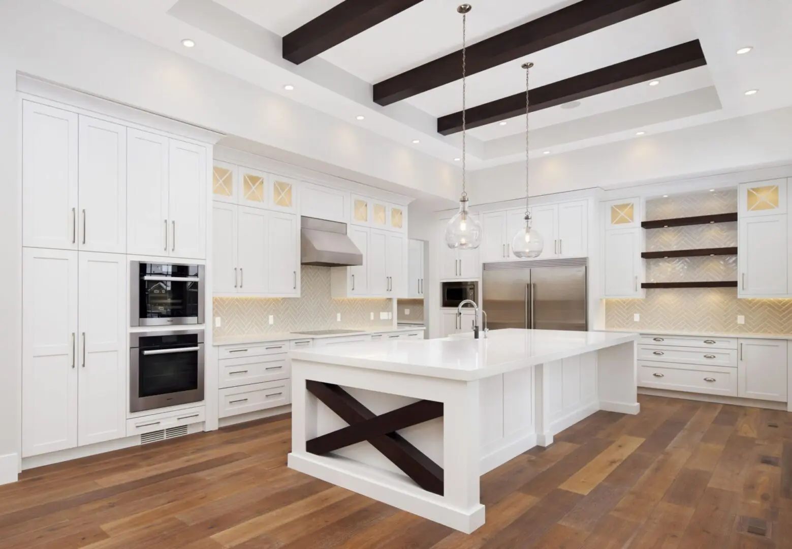 Spacious white kitchen with island, stainless steel appliances, dark wood beams, and hardwood floors.