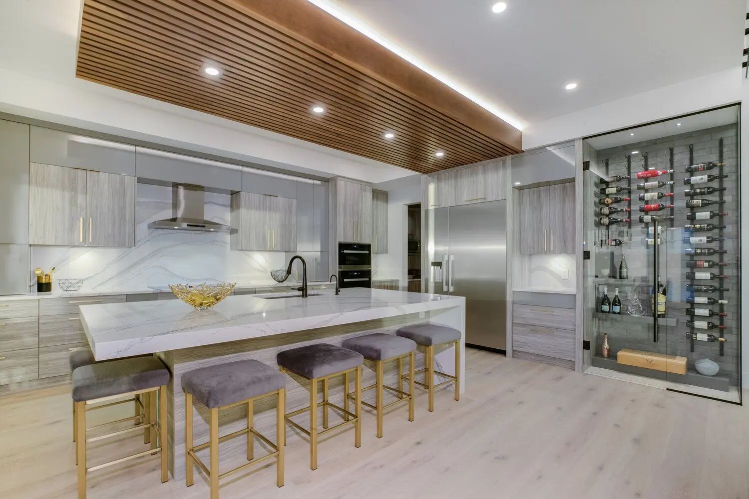 Modern kitchen with light wood ceiling, marble island with stools, and wine storage.