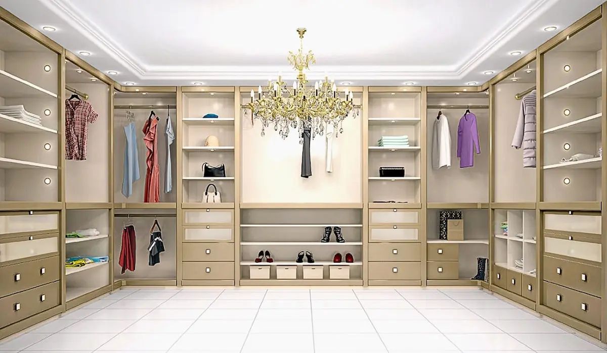 Elegant walk-in closet with beige cabinetry, a chandelier, and hanging clothes and accessories.