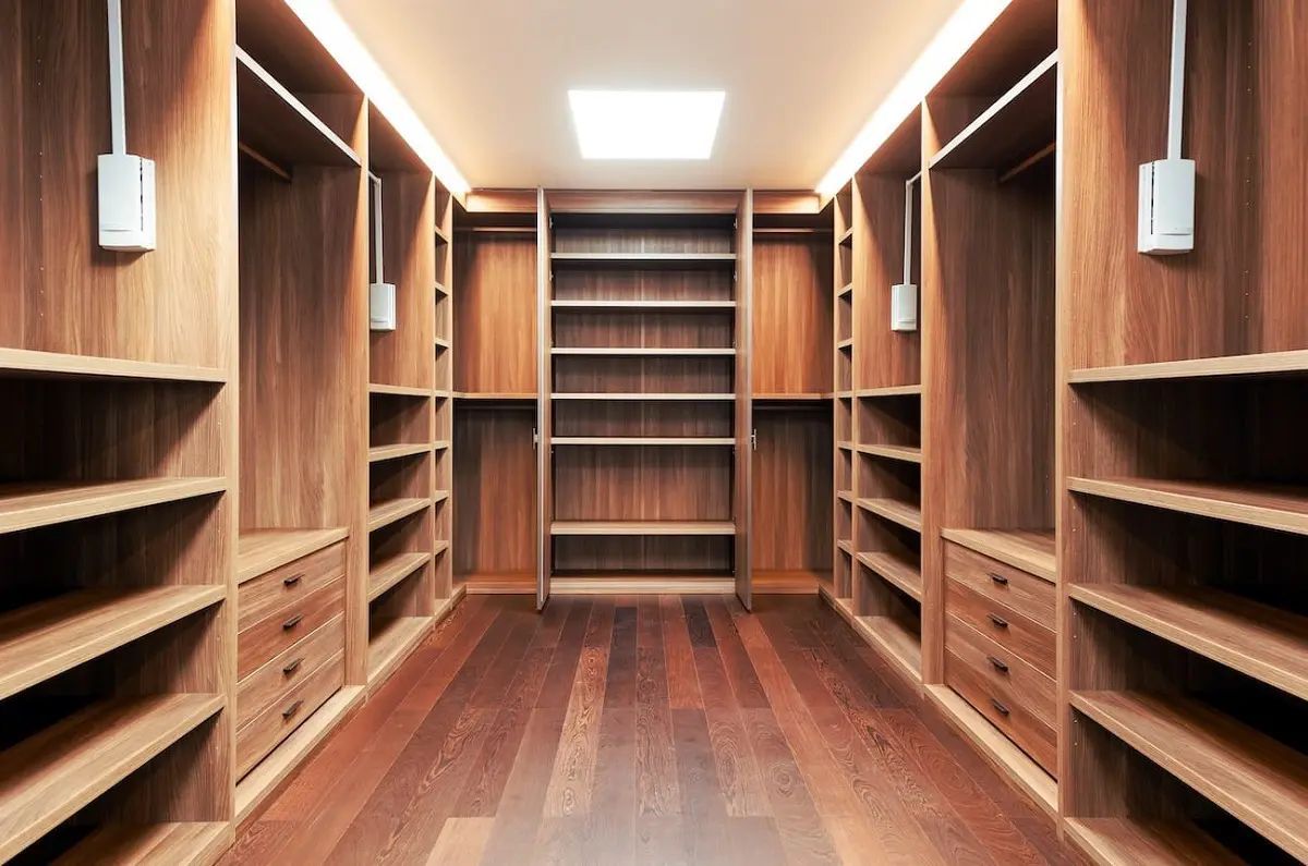 Wooden walk-in closet with shelves, drawers, and lighting. Dark wood floor and walls.