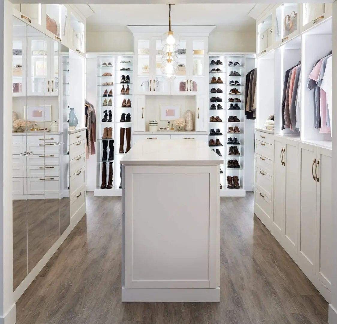 White walk-in closet with island, displaying shoes, clothes, and drawers.