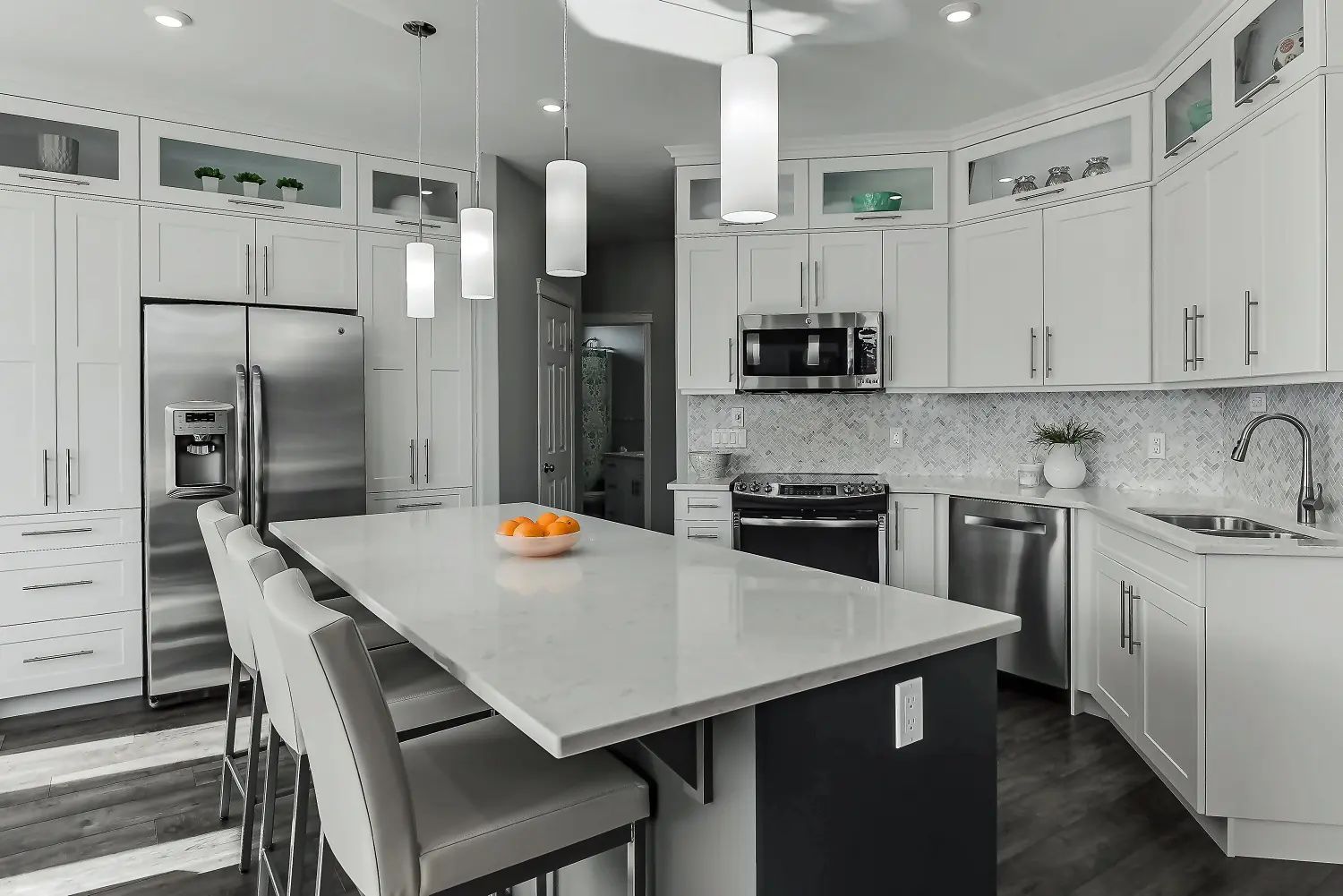 Modern white kitchen with island, stainless steel appliances, and pendant lights.