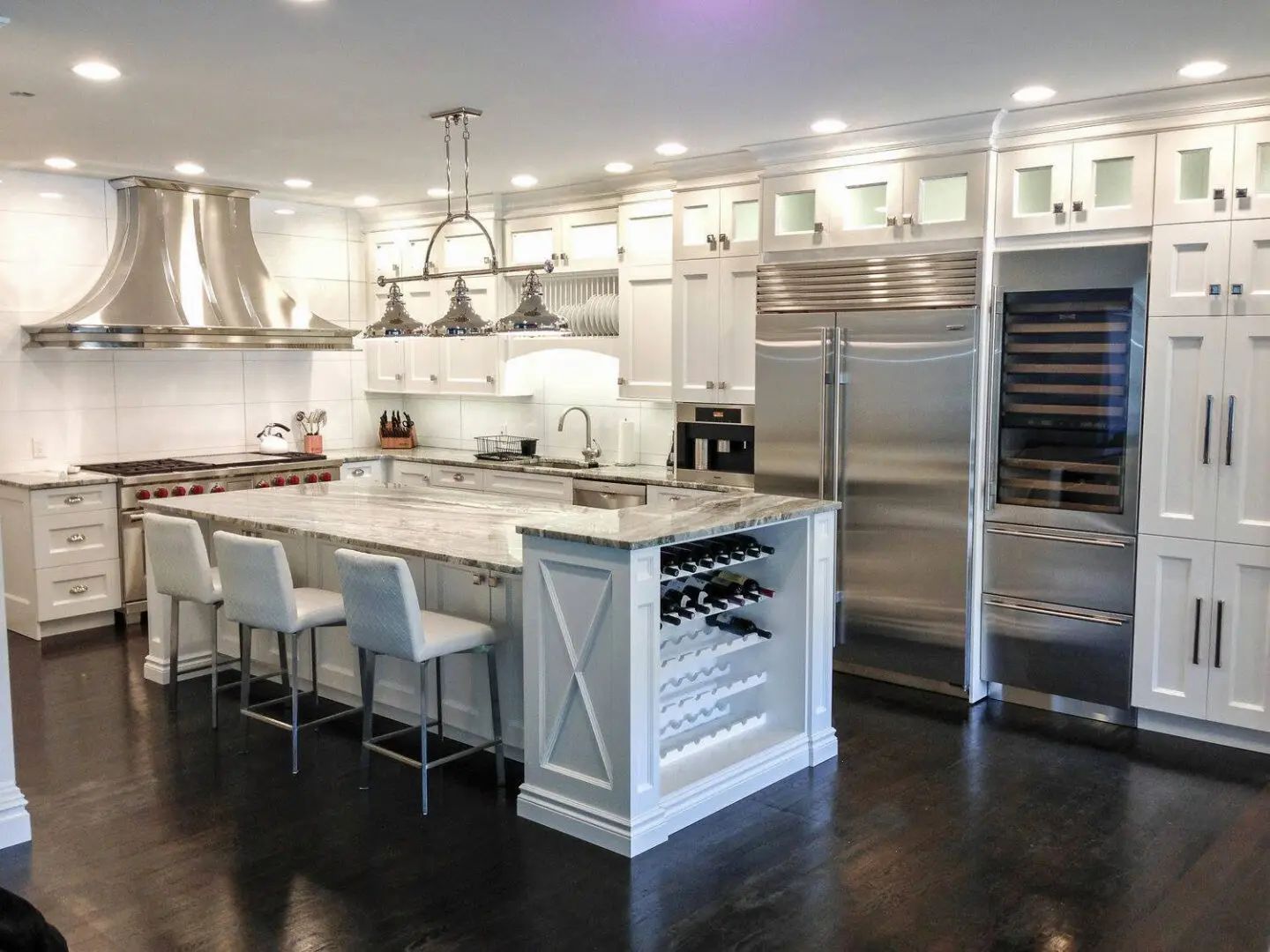 Spacious white kitchen with stainless steel appliances, large island with seating, and dark wood floors.