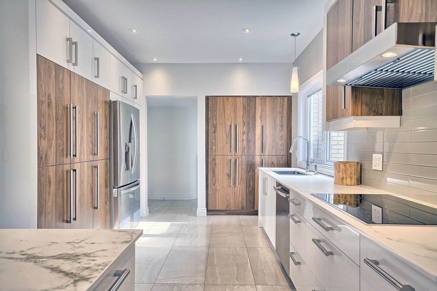 Modern kitchen with light wood and white cabinetry, stainless steel appliances, and a marble countertop.
