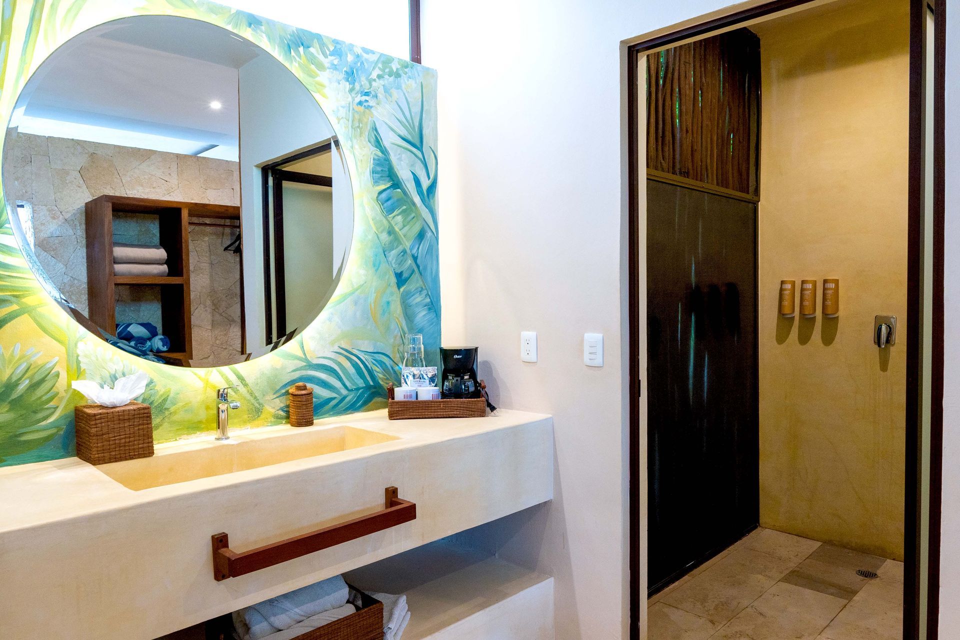 Mueble de baño con espejo redondo de colores, lavabo blanco y puerta abierta a un armario o zona de ducha.