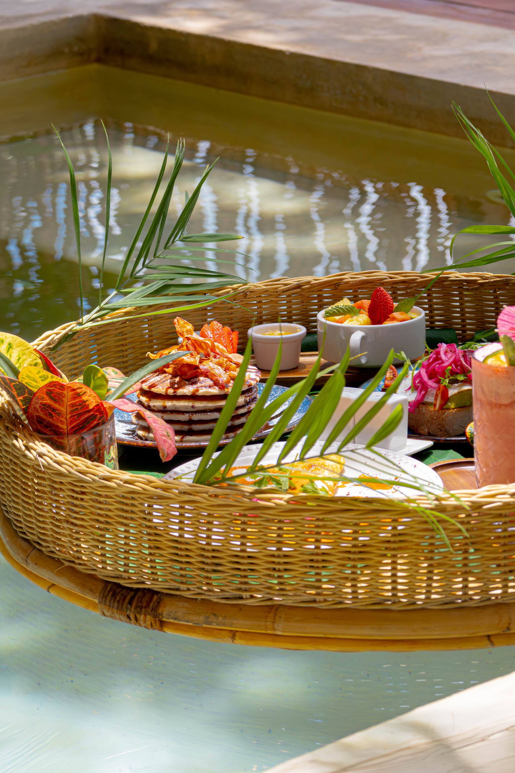 Desayuno flotante servido en la alberca de la villa principal de Khaban Bacalar, con alimentos frescos y un entorno rodeado de naturaleza.