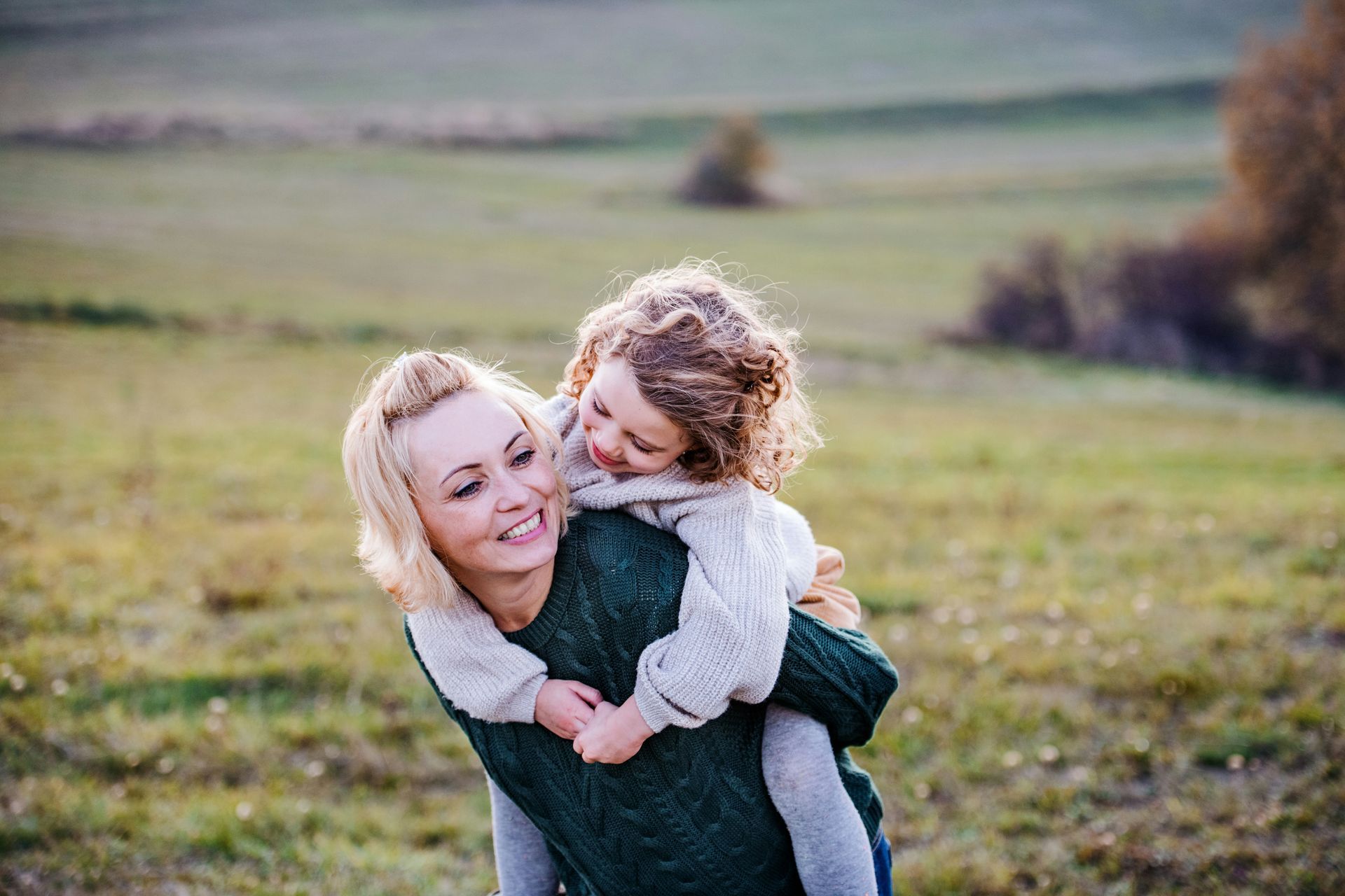 Woman giving a piggyback ride to a young child in a grassy field, smiling.